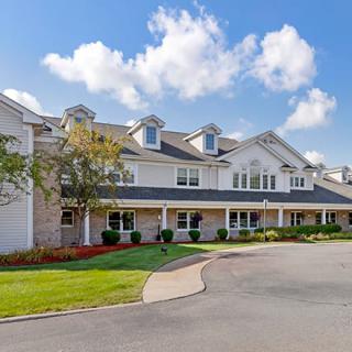 A large residential building with a well-maintained front yard under a partly cloudy sky.