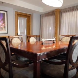 A neatly arranged dining room featuring a polished wooden table and chairs, complemented by curtains and artwork on the wall.