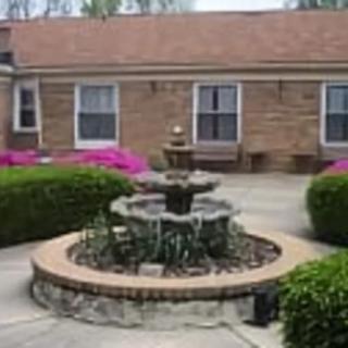 A serene courtyard with a central fountain surrounded by lush greenery and vibrant flowers.