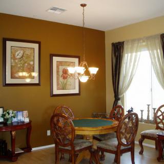 A warmly decorated dining room with a round table, ornate chairs, wall art, and a window with curtains.