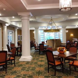 An elegant dining area with columns, chandelier, and carpeted flooring.