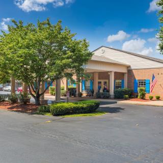 A well-maintained building entrance with a parking lot, surrounded by trees and flags on a partly cloudy day.