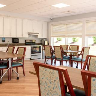 A bright dining area with tables and chairs, adjacent to a kitchen with modern appliances and ample natural light.