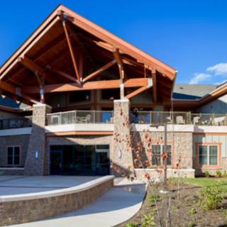 A modern building with a prominent wooden structure and open outdoor space under a clear blue sky.