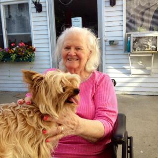 An elderly woman smiling while holding her dog outside.