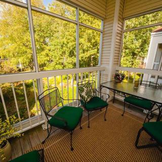 A cozy porch with green cushioned chairs and a glass table, overlooking a lush garden.
