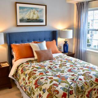 A cozy bedroom featuring a colorful bedspread, decorative pillows, and artwork above the headboard.