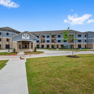 A modern apartment complex with a well-maintained lawn and clear blue sky.