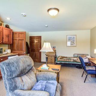 A cozy living space featuring a comfortable chair, bed, desk, and warm lighting.
