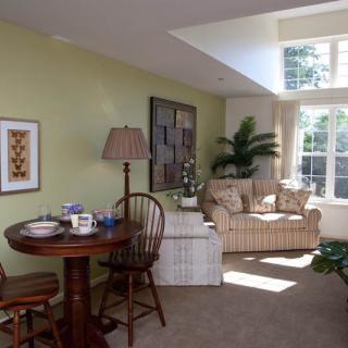 A cozy living room with natural light, featuring comfortable furniture and a small dining area.
