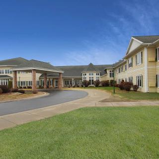 A modern residential building with a well-maintained lawn and a circular driveway under a clear blue sky.