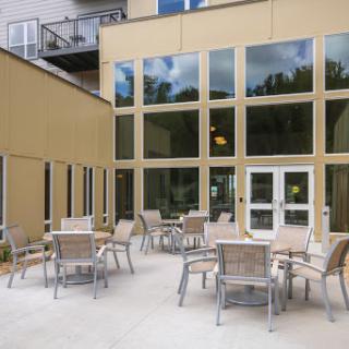 A modern outdoor seating area featuring multiple tables and chairs, surrounded by large glass windows.