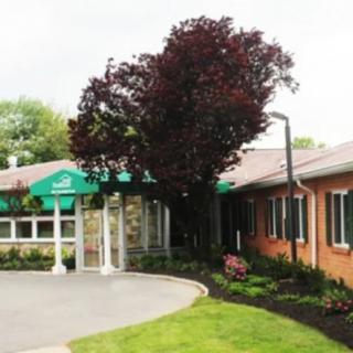 A building entrance with a green awning and surrounding trees and landscaping.