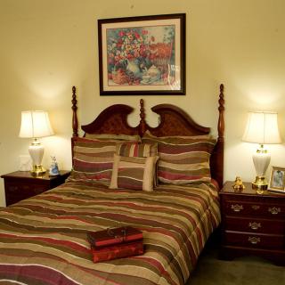 A traditional bedroom with a neatly made bed, flanked by two lamps on nightstands and a painting above the headboard.