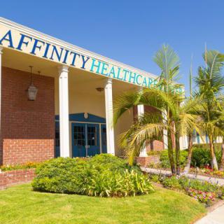 Entrance of a healthcare facility with palm trees and well-maintained landscaping.