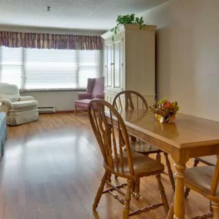 A cozy living room with a wooden dining table and chairs, featuring large windows with curtains.
