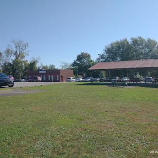 A sunny day showcasing a grassy area in front of a building with parked vehicles.