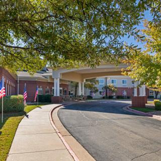 A welcoming entrance to a building with a curved driveway and flags lining the walkway under a sunny sky.