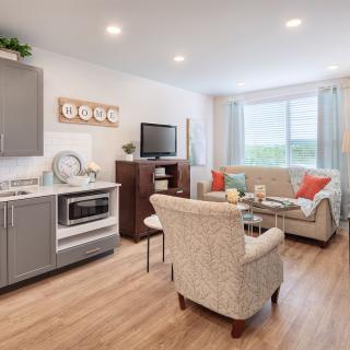 A modern living room with an open floor plan, featuring a kitchenette and cozy seating area bathed in natural light.