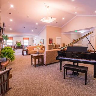A spacious and elegantly furnished living room featuring a grand piano, comfortable seating, and warm lighting.