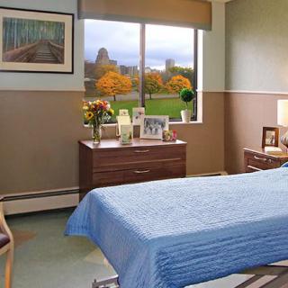 A cozy hospital room with a bed, decorated with flowers and family photos, overlooking a scenic view.