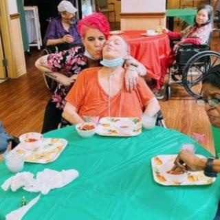 A caregiver showing affection to an elderly person during meal time at a nursing home.