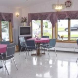 A cozy dining area with round tables and chairs, featuring large windows and a television.