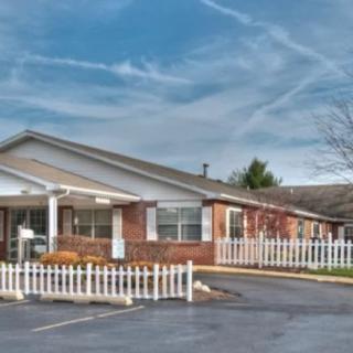 A single-story residential building with a white fence and a parking lot in front under a cloudy sky.