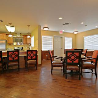A spacious dining area with a kitchen featuring wooden flooring, comfortable chairs, and modern lighting.