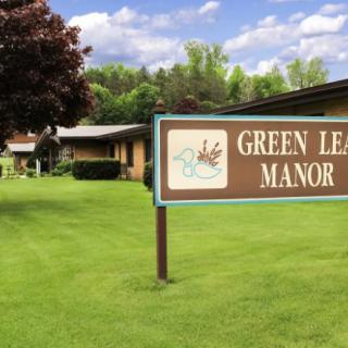 A sign for Green Leaf Manor stands on a well-maintained lawn with trees in the background.