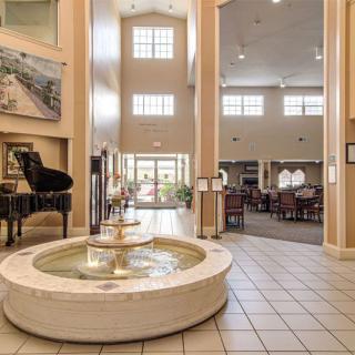 A spacious lobby featuring a central fountain and a grand piano, illuminated by large windows.