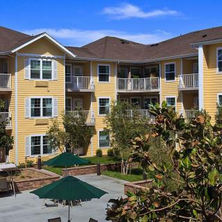 A sunny day view of a yellow apartment building with balconies and outdoor seating areas.