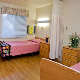 A well-lit hospital room with two beds, each equipped with pink bedding and a curtain divider for privacy.
