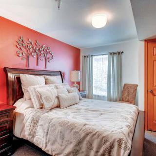 A cozy bedroom featuring a bed with patterned bedding and a decorative headboard against a bold red accent wall.
