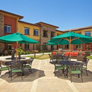 A sunny courtyard with tables and green umbrellas in front of a colorful building.