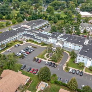 Aerial view of a residential complex with a parking lot surrounded by trees in a suburban area.