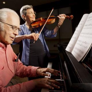 Two elderly musicians performing a duet with piano and violin.