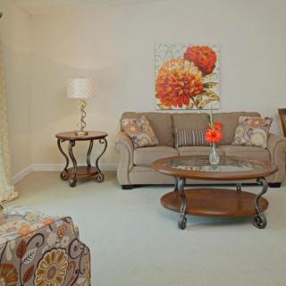 A cozy living room with a sofa, coffee table, lamp, and floral artwork on the wall.