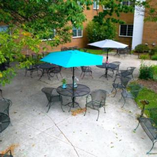 An outdoor patio area with tables, chairs, and umbrellas surrounded by greenery.