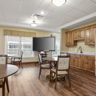 A cozy dining area with a kitchenette and television, featuring wooden furniture and a hardwood floor.