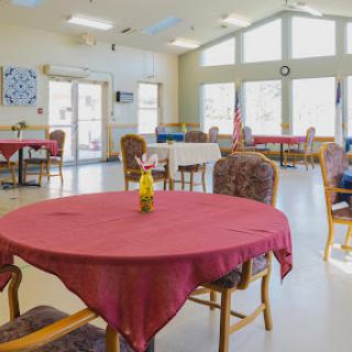A bright and inviting dining area featuring round tables with red tablecloths, surrounded by comfortable chairs and decorated with flowers.