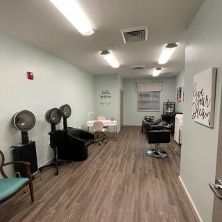 A cozy salon interior with hair dryers, chairs, and soft lighting.