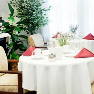 A elegantly set table in a restaurant with red napkins and greenery in the background.