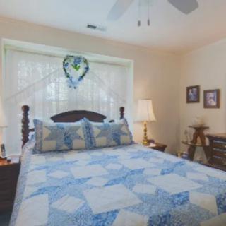 A cozy bedroom featuring a bed with a blue and white quilt, flanked by two lamps and decorated with wall art.