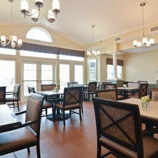 A well-lit dining room with multiple tables and chairs, featuring large windows and elegant chandeliers.