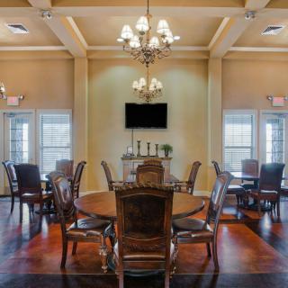 A spacious dining room featuring elegant chandeliers, round tables, and wooden chairs set on a polished wooden floor.