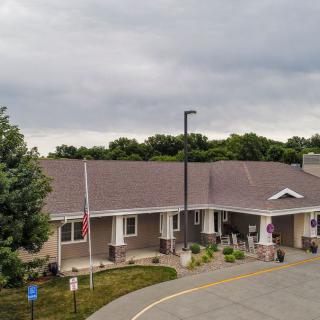 A building with a flagpole and landscaped entrance under a cloudy sky.