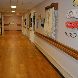 A long hallway in a nursing home with wooden flooring and wall decorations.