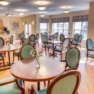 A bright and spacious dining room with multiple tables and chairs, featuring large windows and elegant decor.