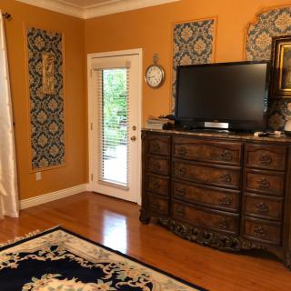 A cozy living room with orange walls, featuring a large wooden dresser and television, complemented by decorative wall art and a patterned rug.